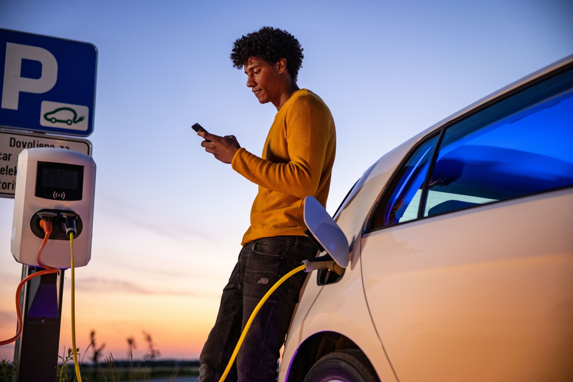 Man using mobile phone while charging electric car