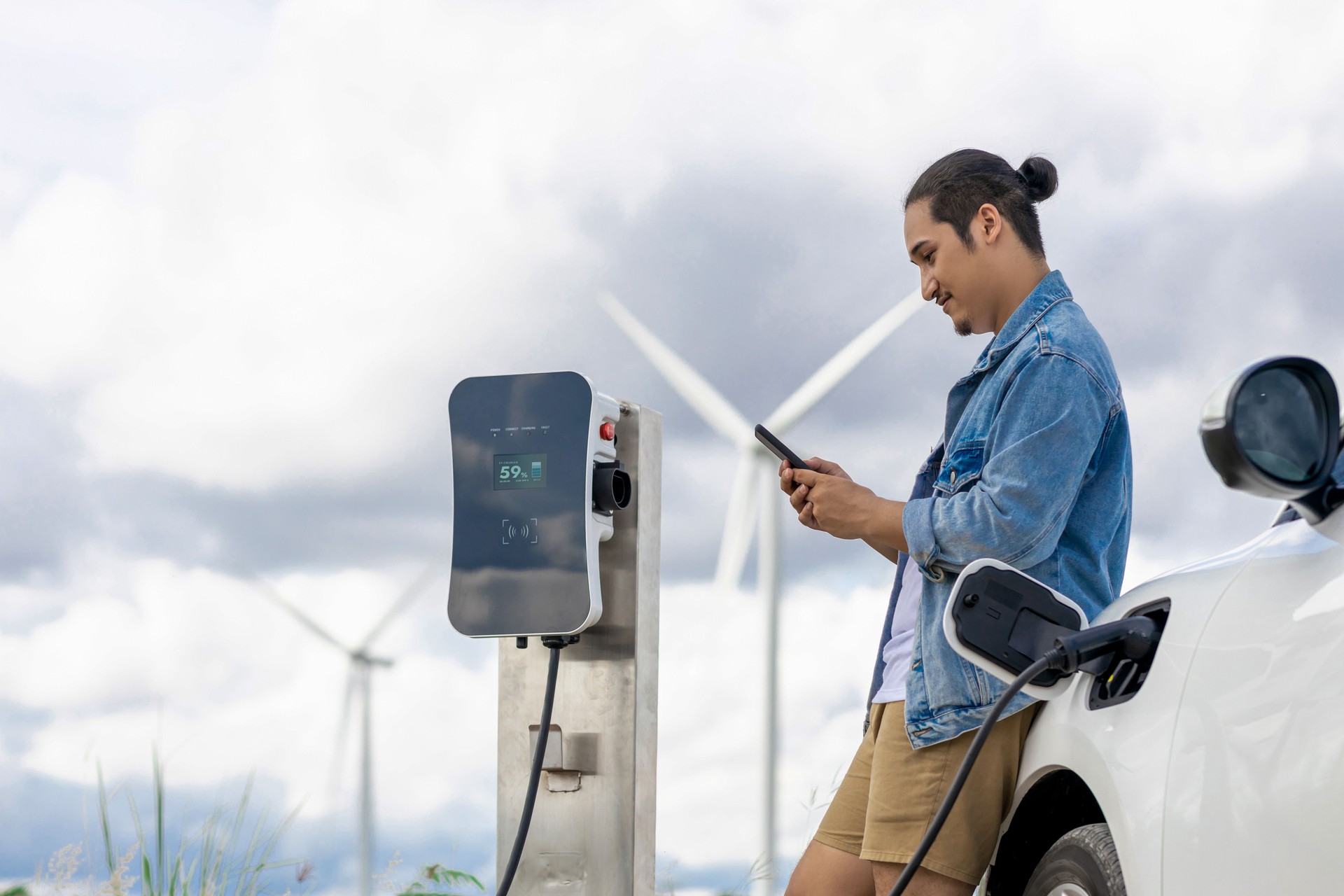 Progressive man with his EV car and wind turbine as concept of renewable energy.