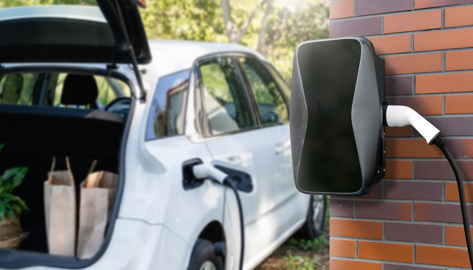Charging electric car next to house with charging station on the wall