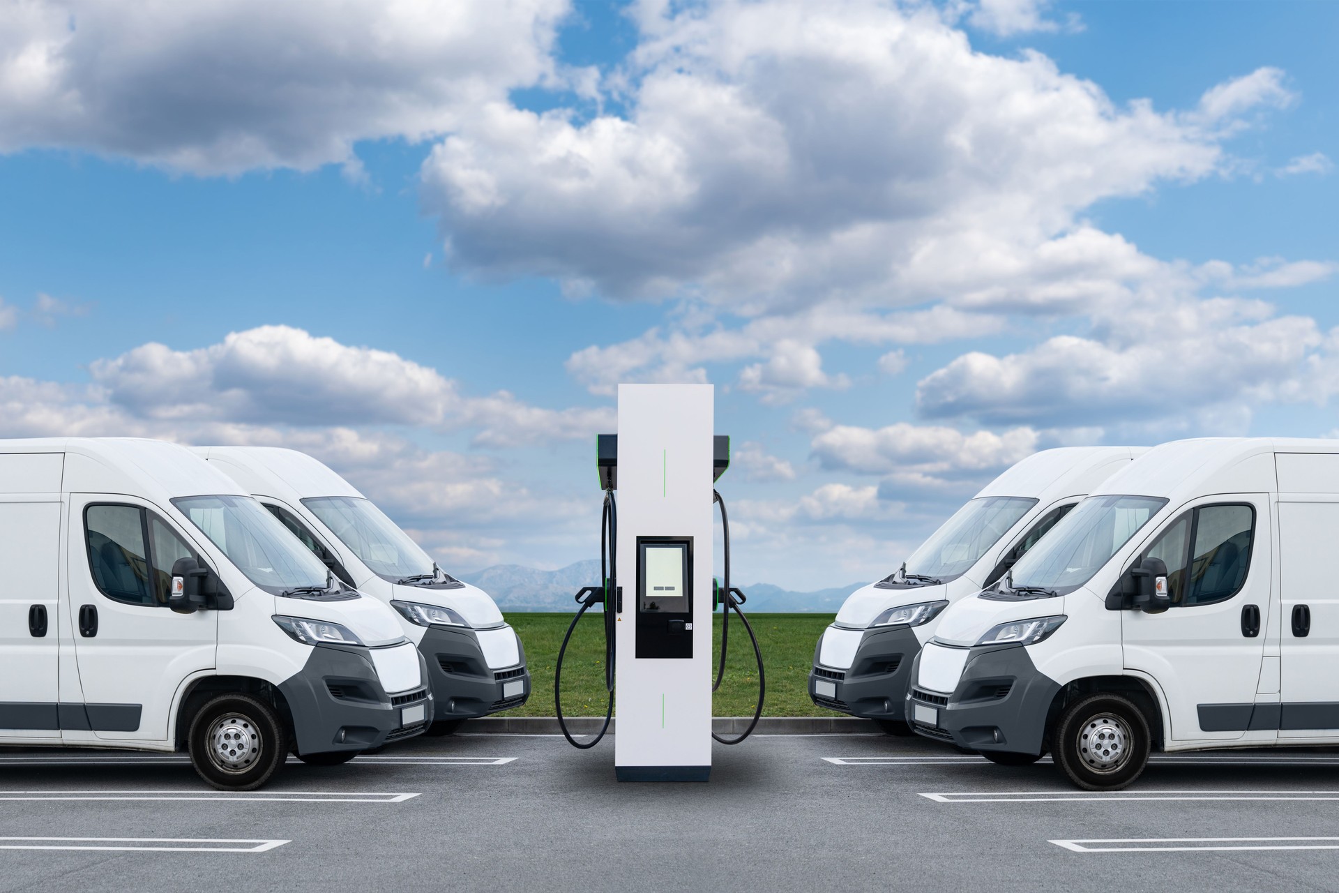 Electric delivery vans are parked in rows nearly by electric charging station. Commercial fleet.